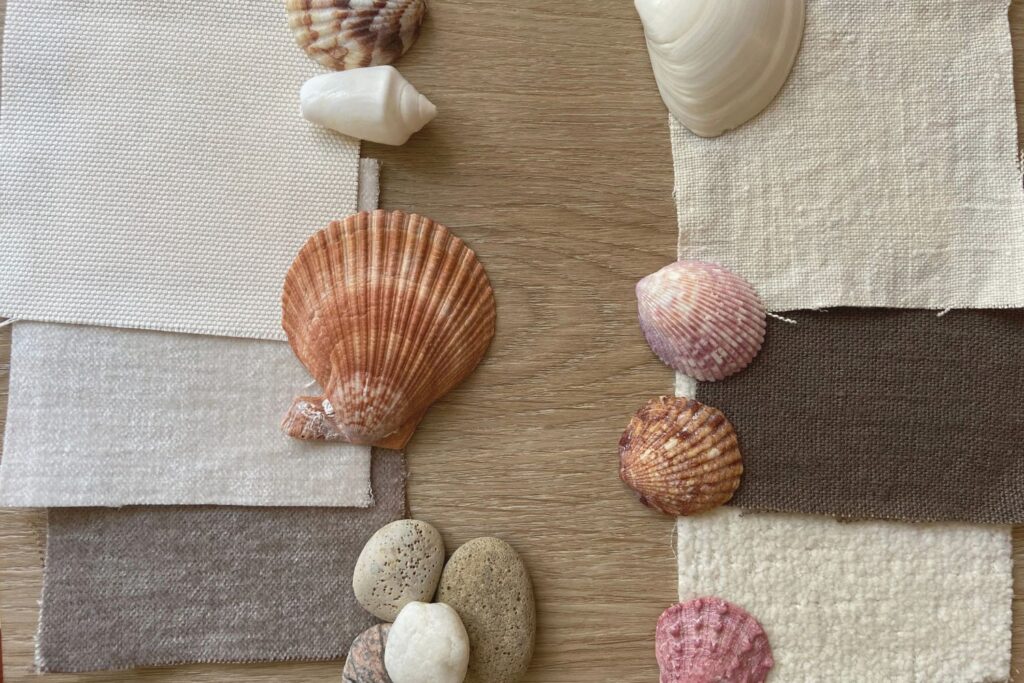 Fabric swatches and seashells arranged on an oak plank as a cottage renovation moodboard.